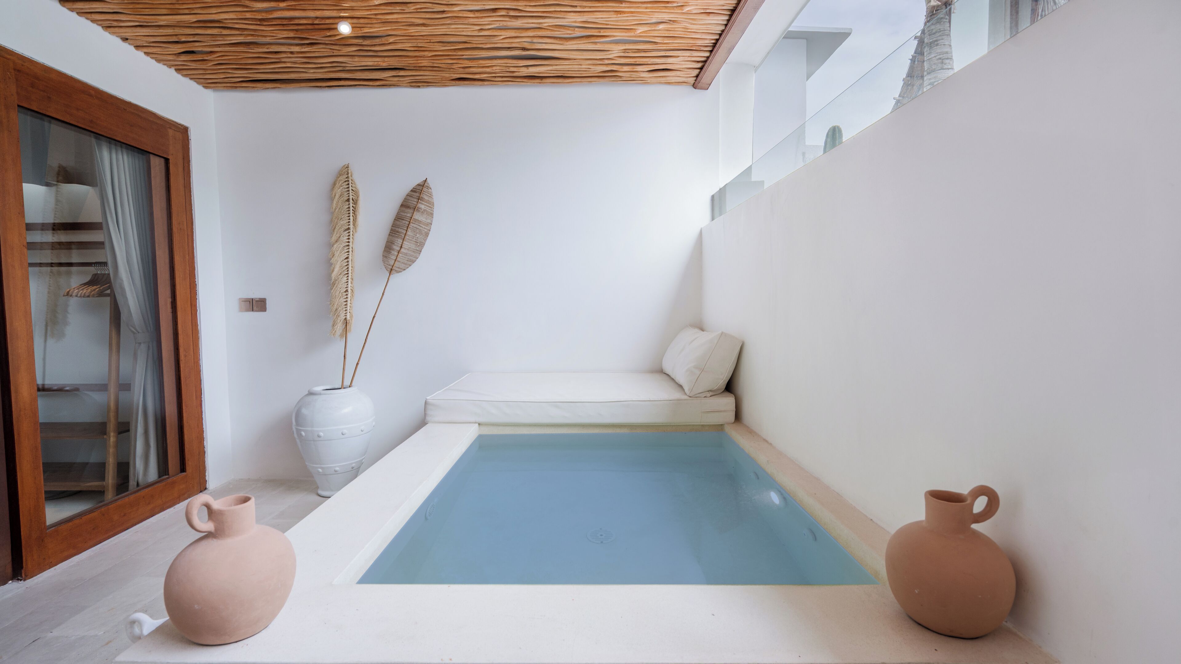 Ein moderner, minimalistisch gestalteter Innenbereich mit Pool, weißen Wänden, einer Sitzecke und zwei großen Vasen.