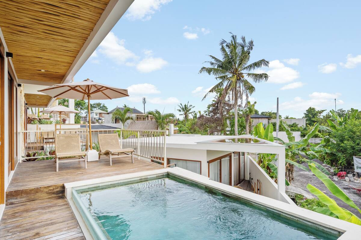Ein Poolbereich mit Holzterrasse, Liegestühlen und Sonnenschirmen.