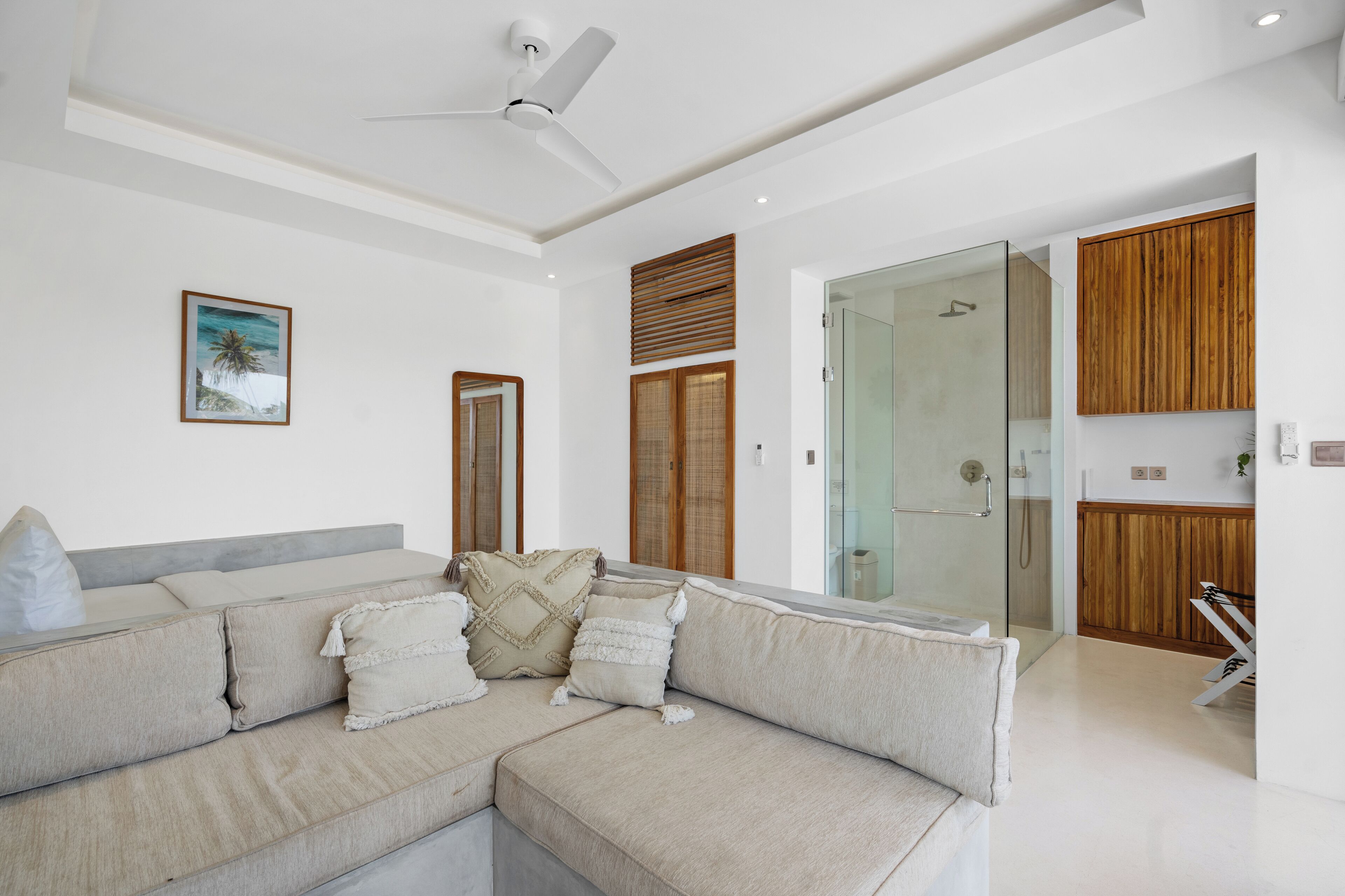 Uma sala de estar moderna com sofá modular, ventilador de teto, box de vidro para chuveiro e armários de madeira.
