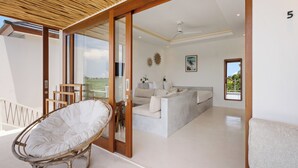 Un amplio salón con un gran ventanal, un sofá, un sillón y un ventilador de techo.