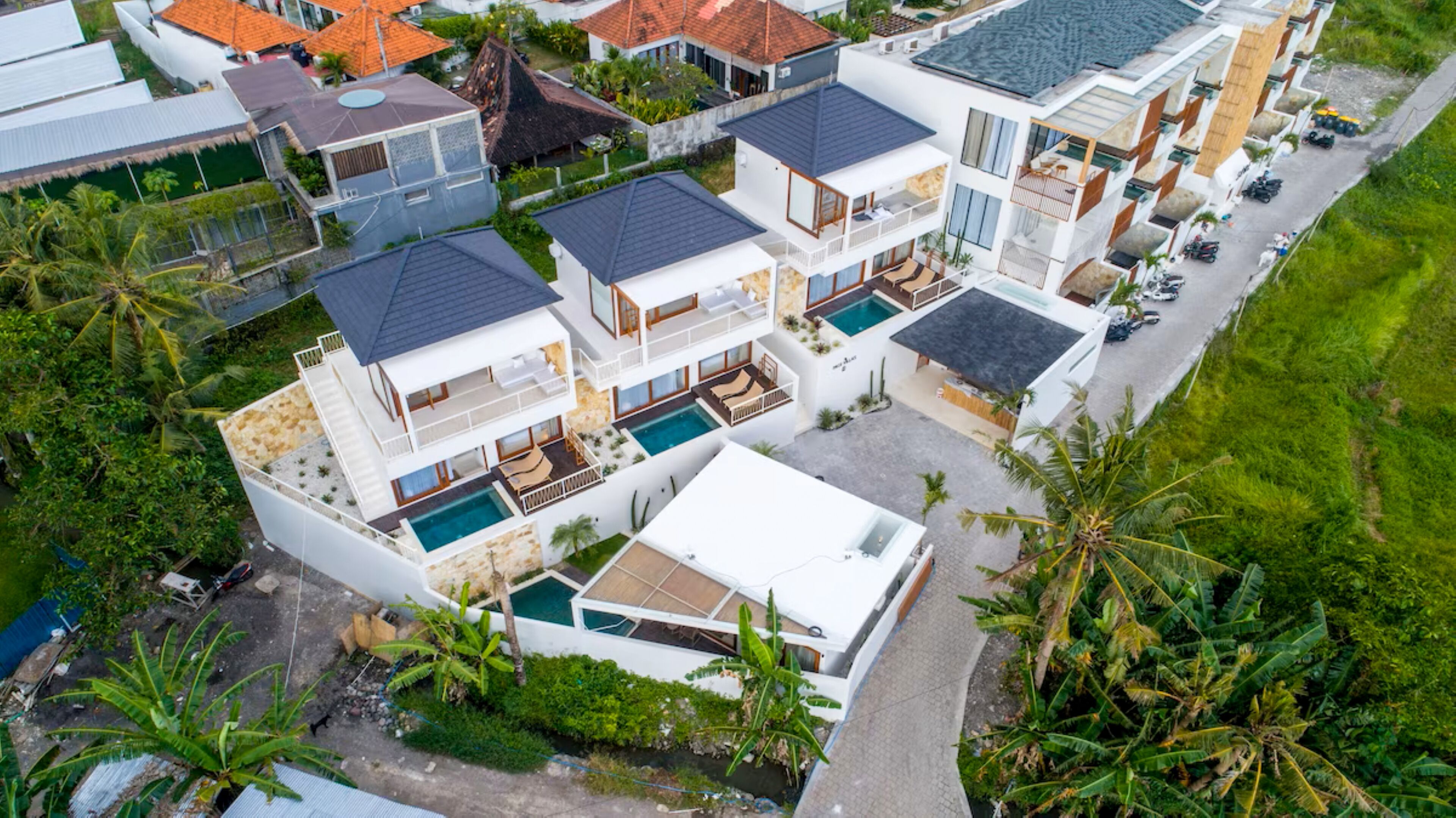 Un immeuble résidentiel moderne à plusieurs étages, doté d’une piscine, entouré d’une végétation luxuriante et de palmiers.