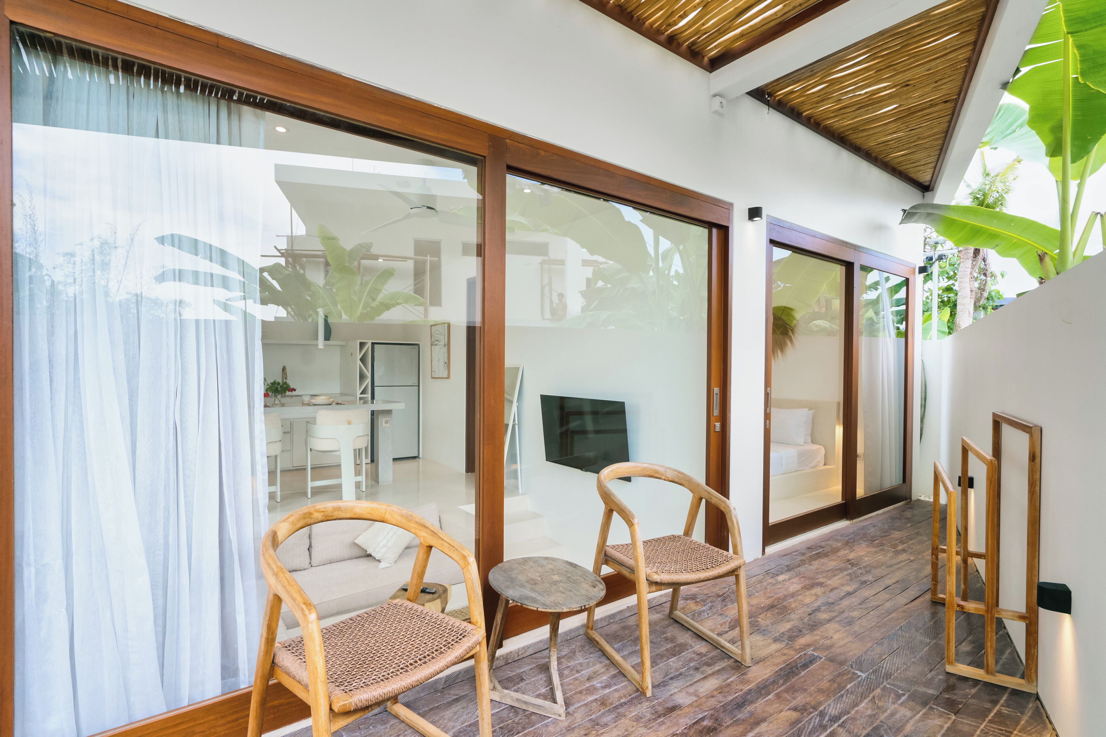 A modern interior with sliding glass doors leading to a dining area, wicker chairs, and a flat-screen TV.