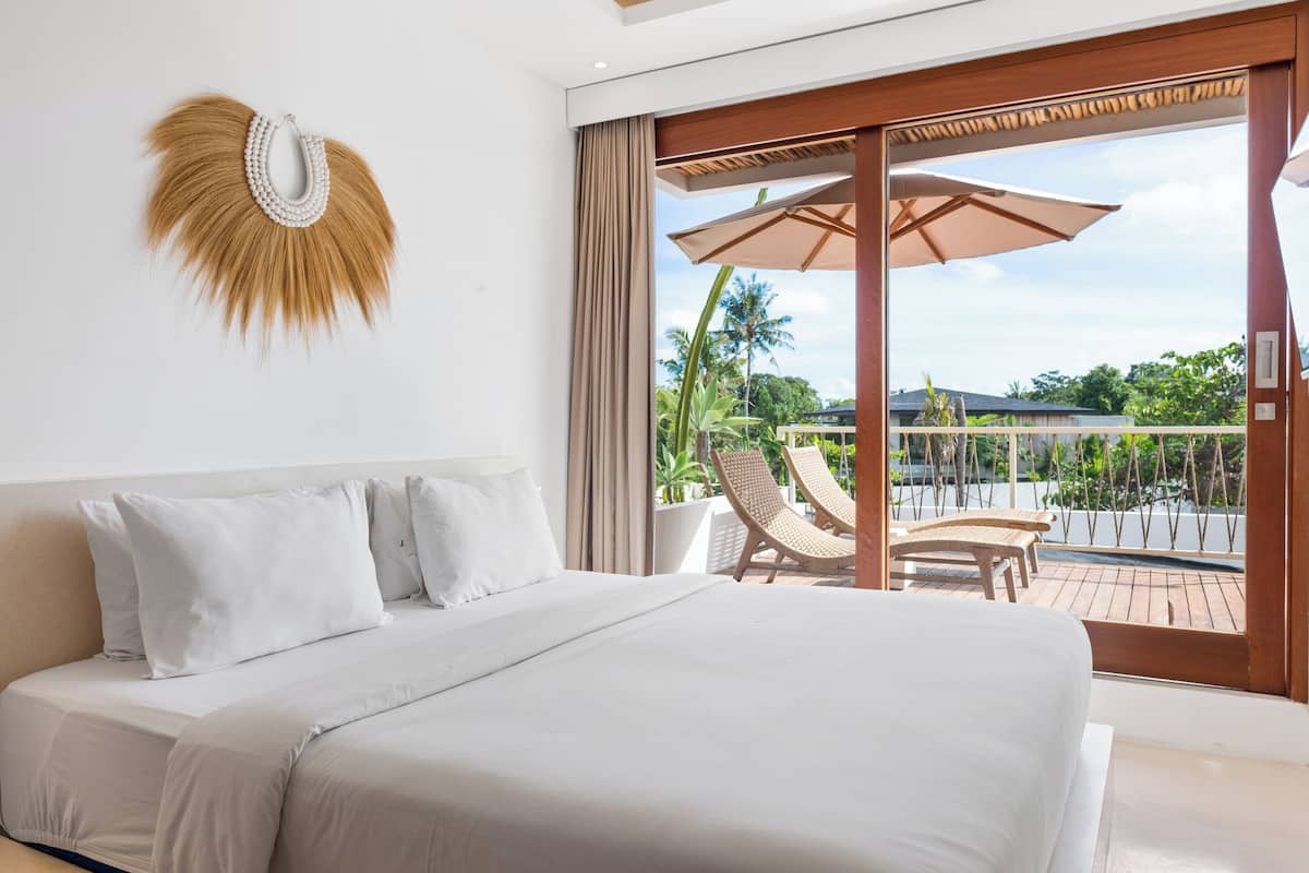 Ein Schlafzimmer mit einem großen Bett, Blick auf den Balkon und zwei Sessel.