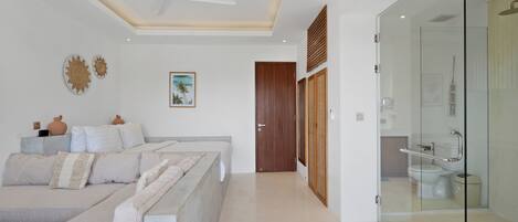 A modern bedroom with a sofa, a ceiling fan, and a glass shower enclosure.