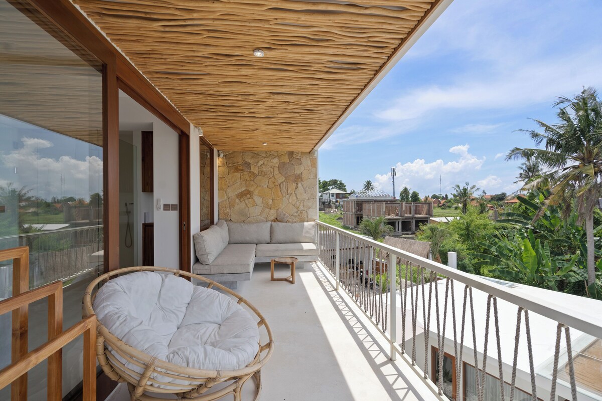 A balcony with a wicker chair, a sofa, and a stone wall.