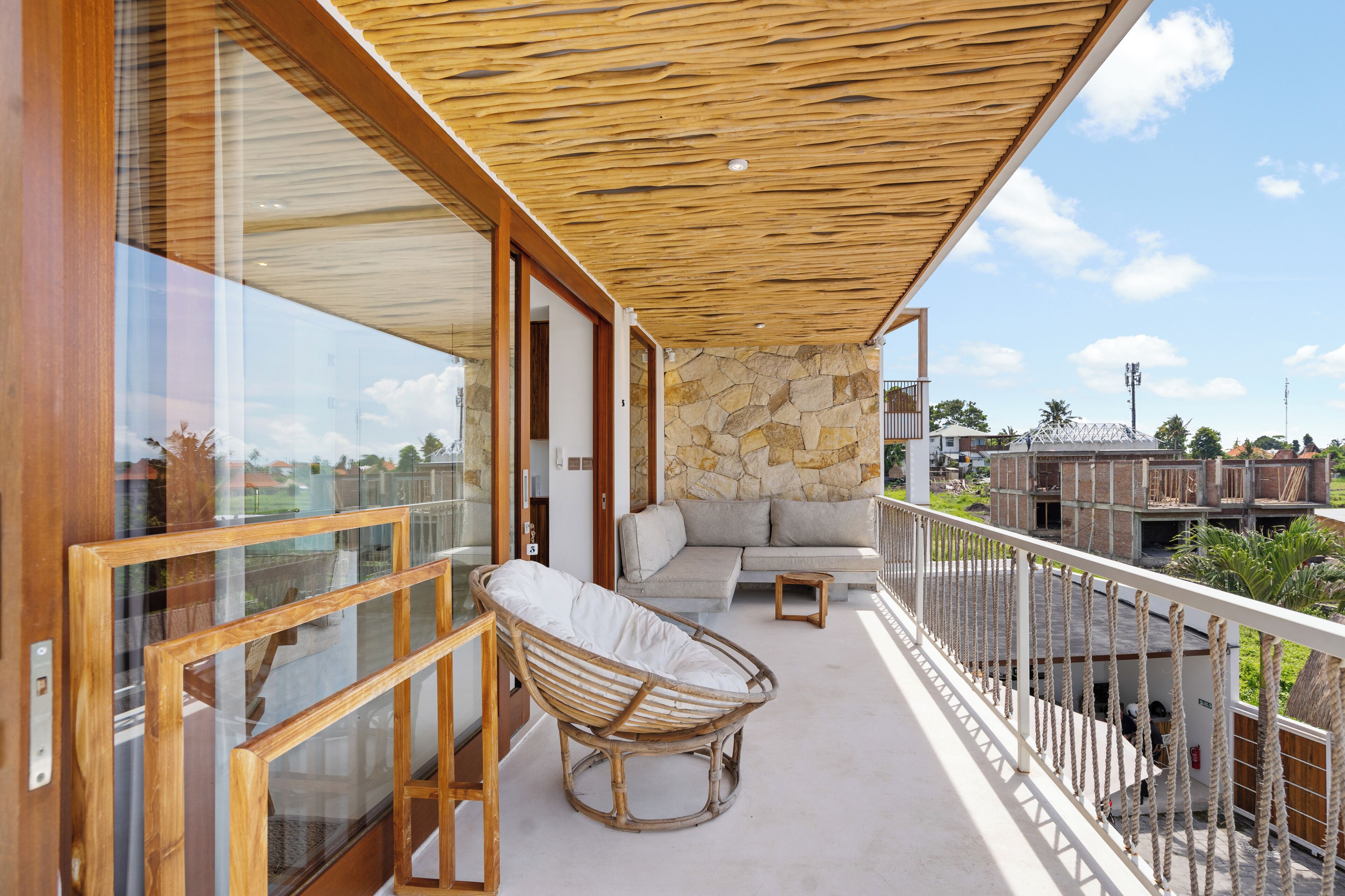 A balcony with a stone wall, a wicker chair, and a sofa.