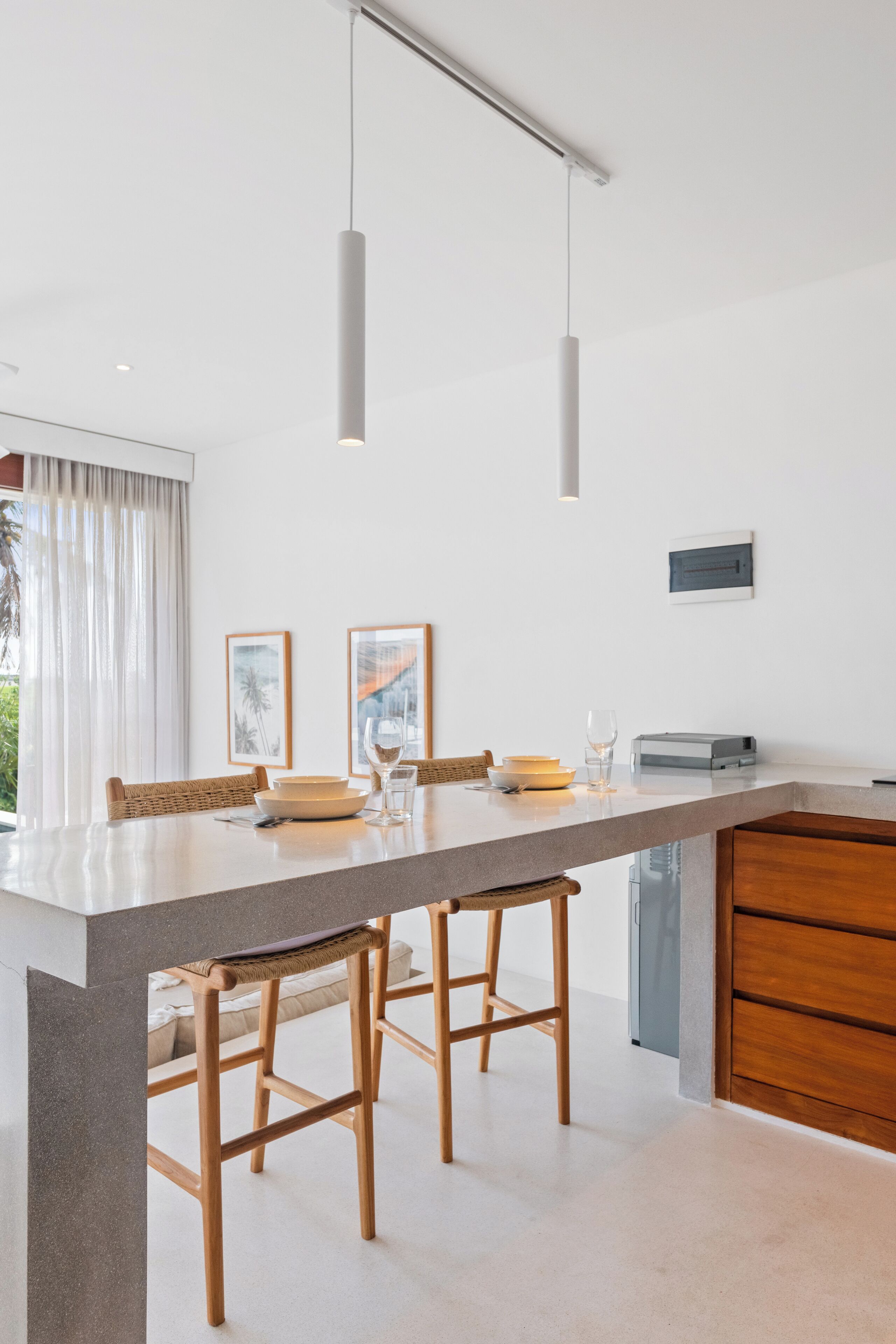 A modern kitchen with a central island, wooden bar stools, pendant lighting, and framed artwork on the wall.
