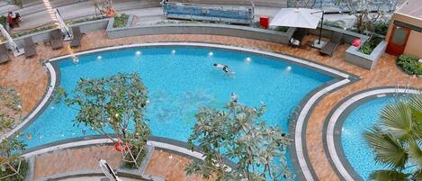 A large indoor swimming pool with a curved design, surrounded by lounge areas and palm trees.