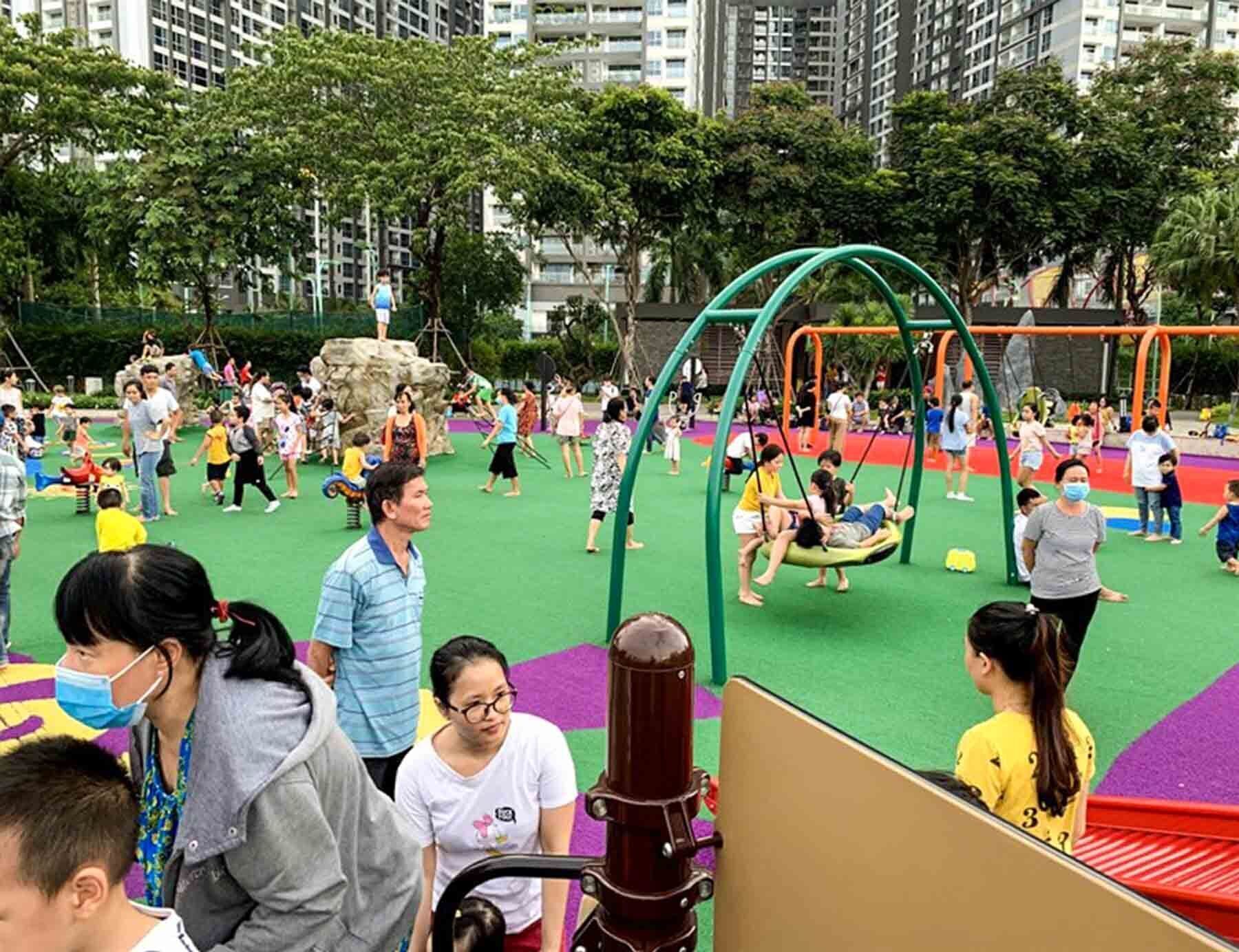 A playground with swings and climbing structures surrounded by greenery and buildings.