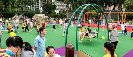 A playground with swings and climbing structures surrounded by greenery and buildings.