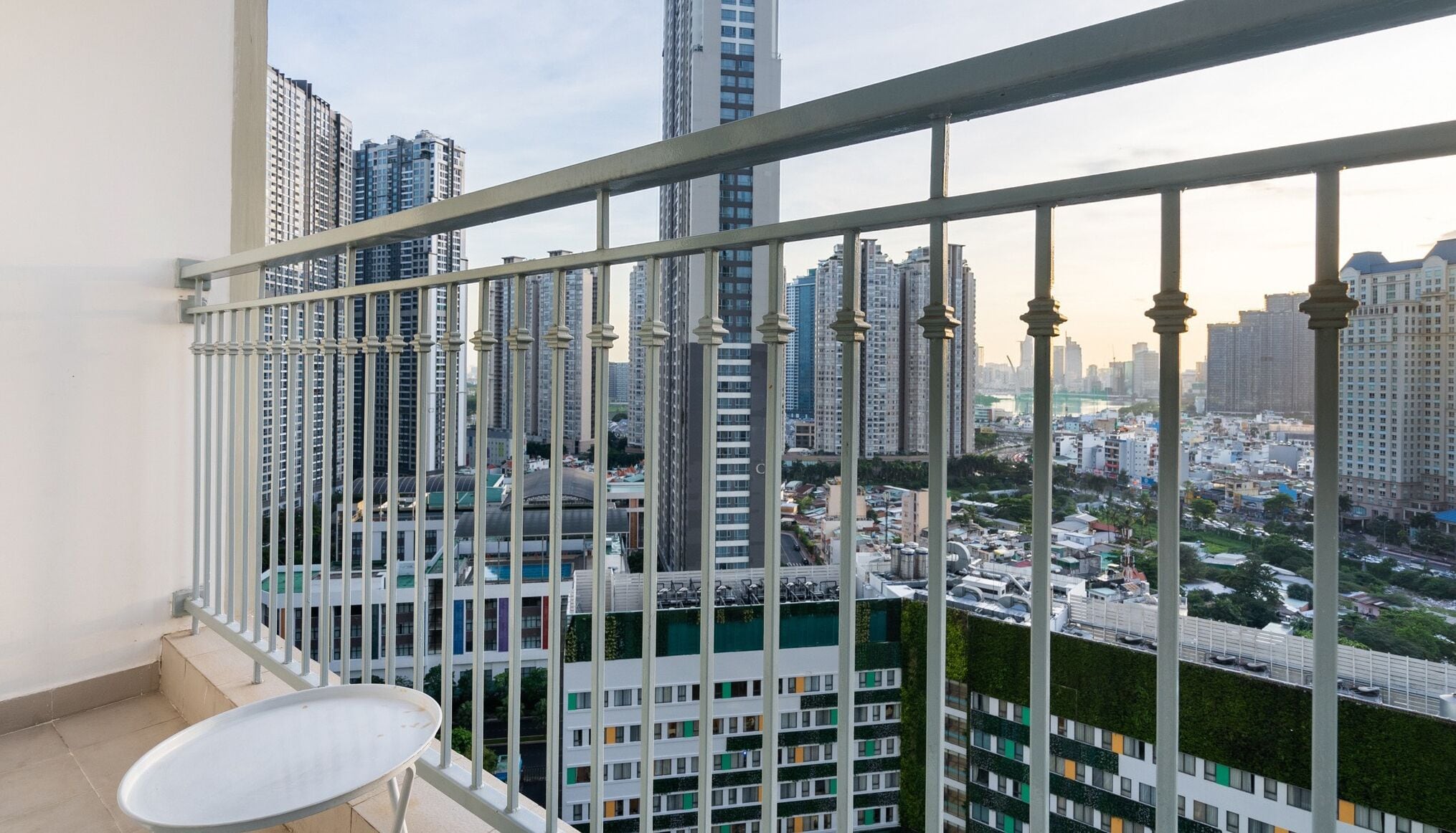 Un balcon doté d’une rambarde en métal, d’où l’on peut admirer un paysage urbain avec de nombreux immeubles de grande hauteur.