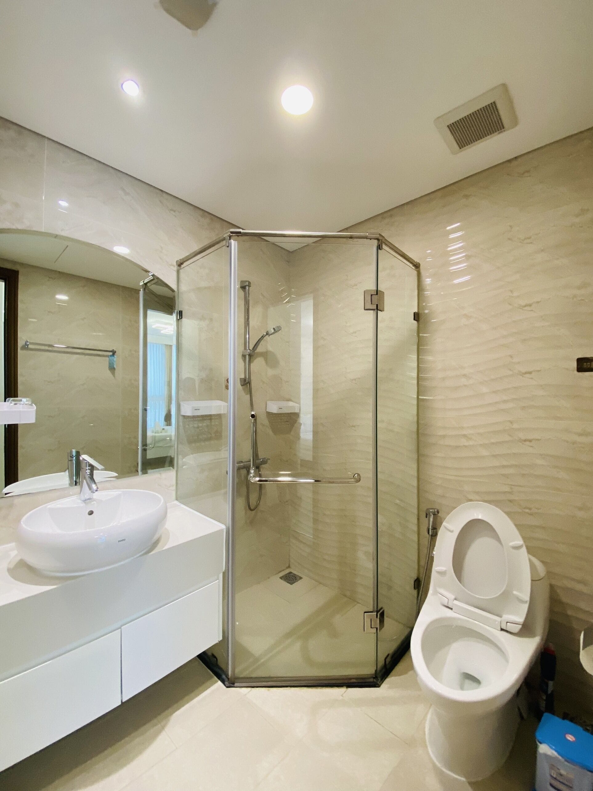 A modern bathroom with a glass-enclosed shower, a white sink, and a toilet.