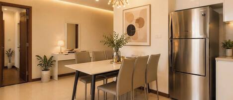 A modern kitchen with a stainless steel refrigerator, a dining table with chairs, a chandelier, and a potted plant.