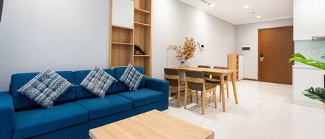 Un salon moderne avec un canapé bleu, une table basse en bois et un coin repas comprenant une table et des chaises en bois.