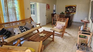 Un accogliente soggiorno con un divano in legno, poltrone e un tavolino. C'è anche una zona pranzo con tavolo e sedie, e un televisore su un mobile in legno.