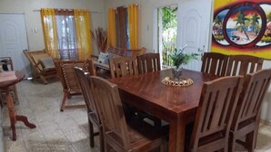 Zona pranzo con tavolo e sedie in legno, tende gialle e un murale tropicale sulla parete.