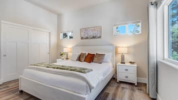 A bedroom with a large bed, two bedside tables, a ceiling fan, and a window with curtains.