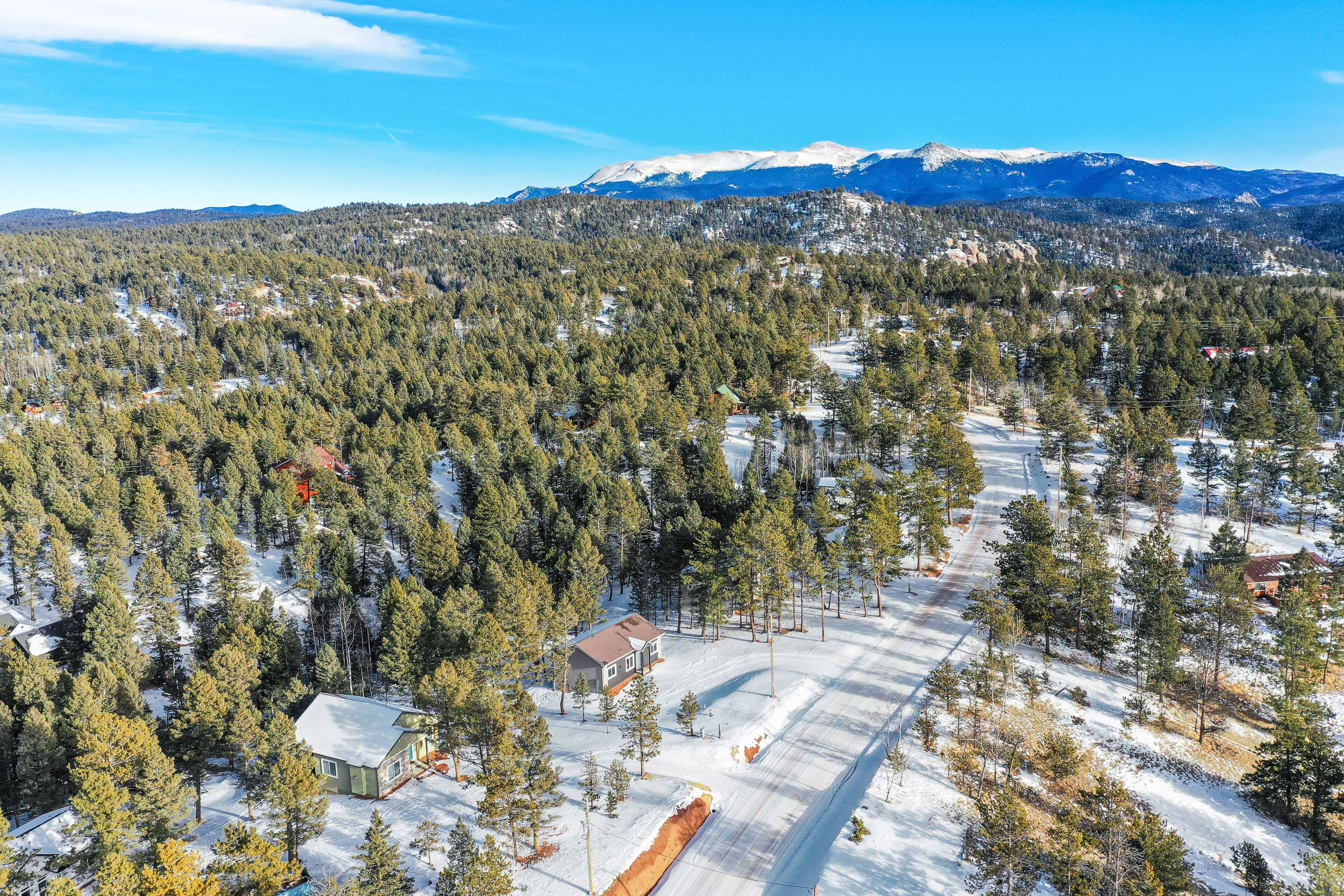 Une cabane isolée, entourée d’une forêt dense et d’un paysage enneigé, offrant une vue dégagée sur les montagnes lointaines.