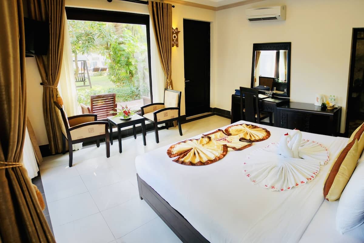 Habitación de hotel con cama, escritorio, silla, televisor y vistas al jardín.