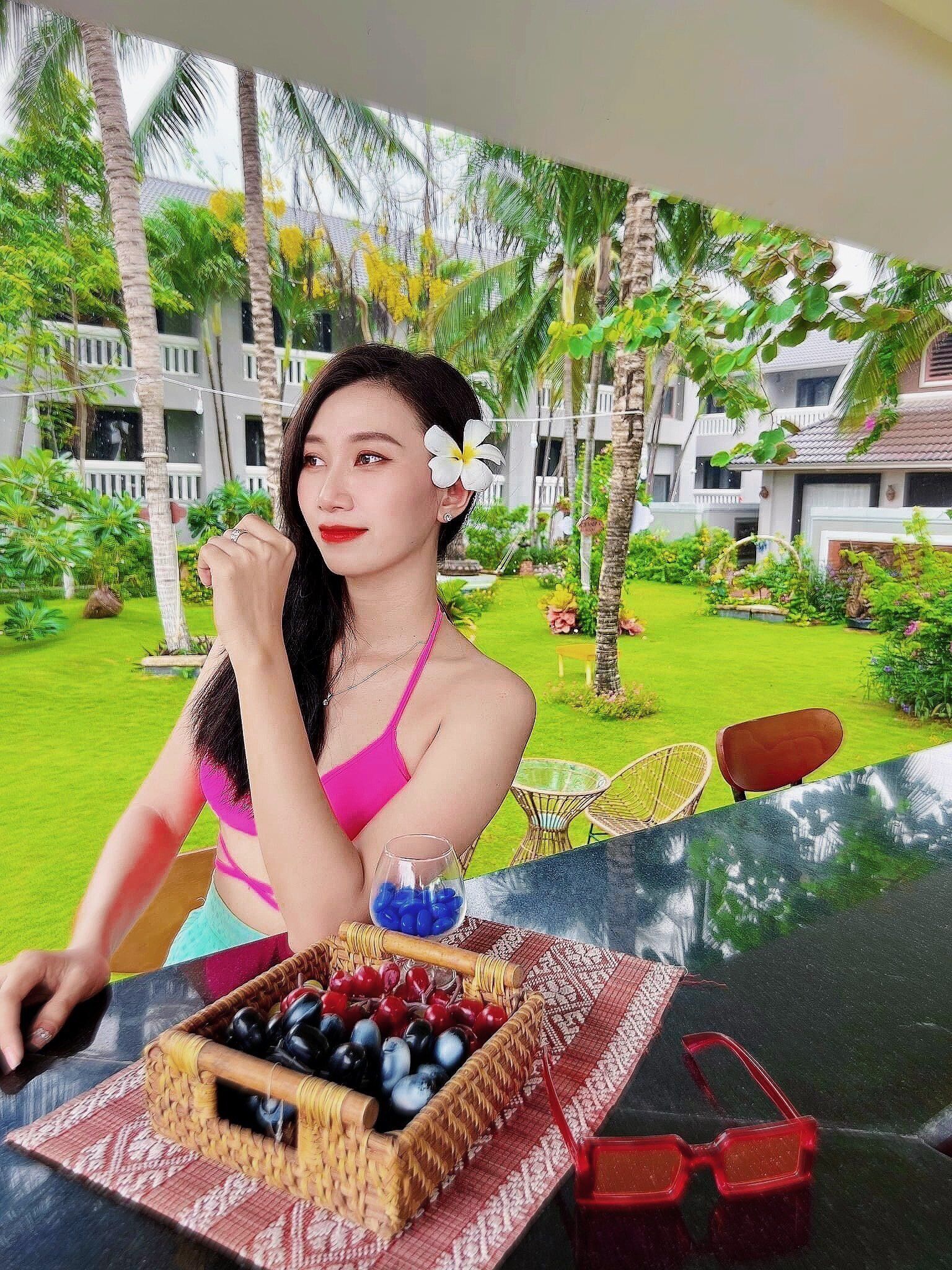 A person seated at an outdoor table with a tropical garden view, a wicker basket of fruits, and a pair of sunglasses on the table.