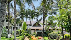 Un jardín exuberante con palmeras, una piscina y zonas de estar al aire libre.