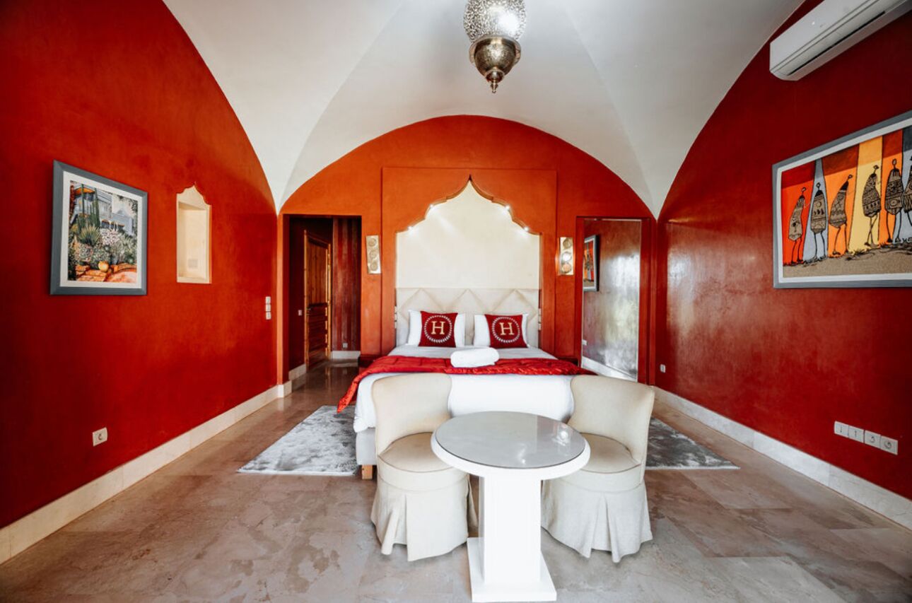 Une chambre d’hôtel avec un grand lit, un coin salon avec une table et des murs rouges.