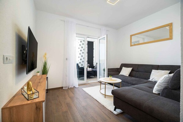 A modern living room with a dark grey sofa, a flat-screen TV, a wooden side table, and a round coffee table.
