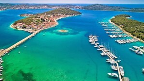 Vue aérienne d’une zone côtière avec un port de plaisance, des eaux turquoise et limpides, et une petite île avec des bâtiments.