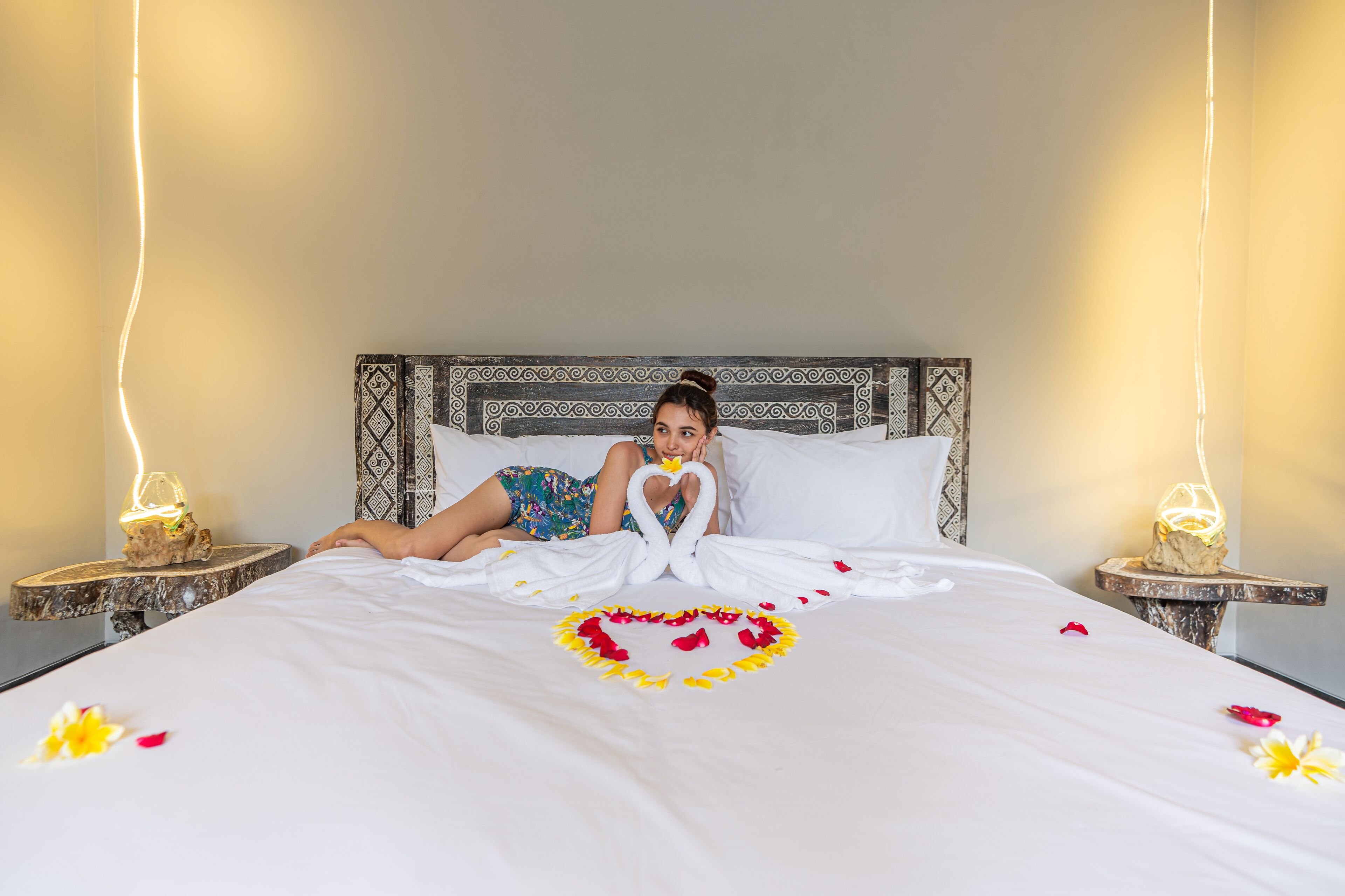 A bed with a heart-shaped flower arrangement, swans made of towels, and a person holding a heart-shaped object.