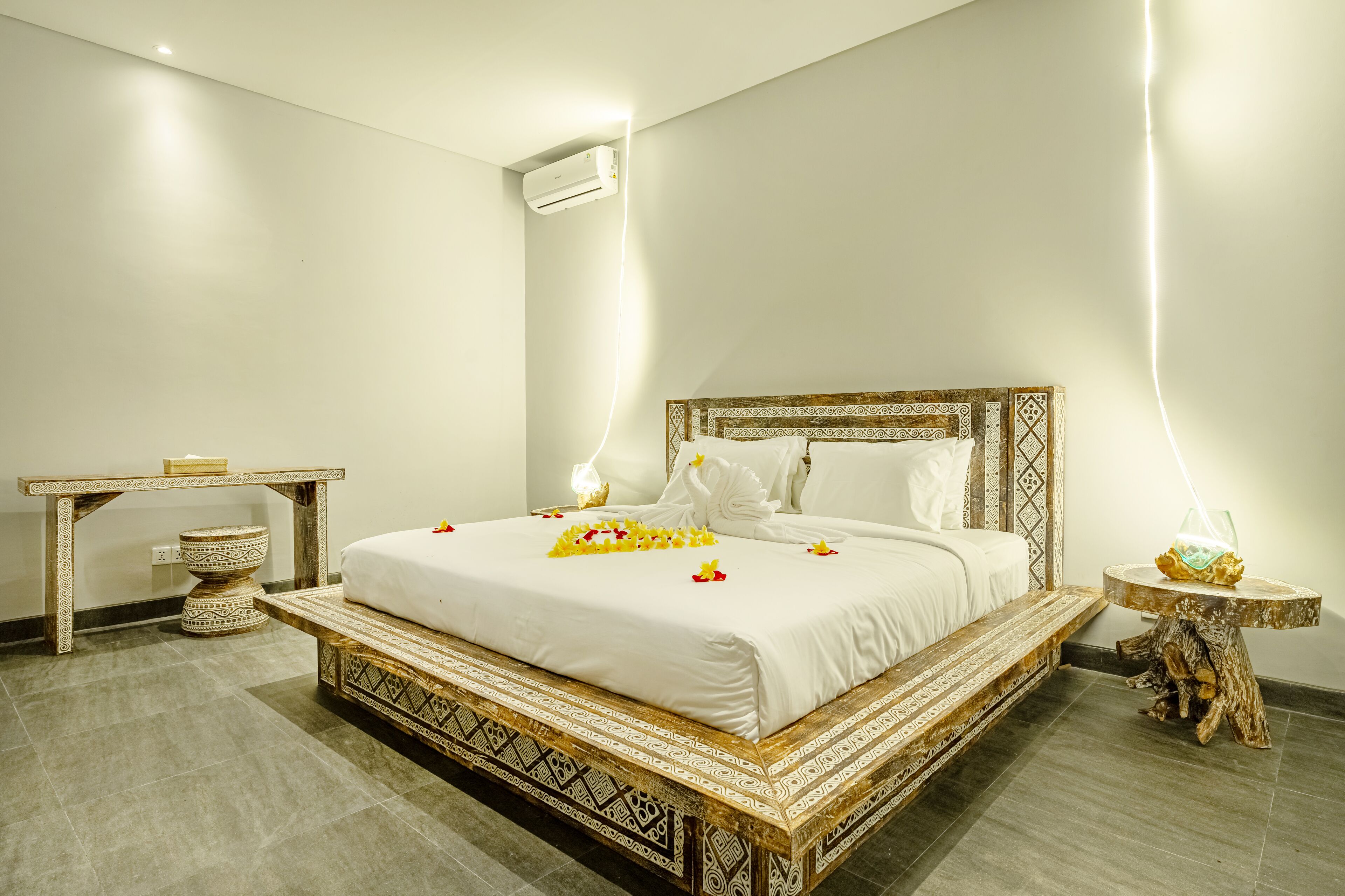 A spacious bedroom with a large bed, a bedside table, a nightstand, and an air conditioning unit.