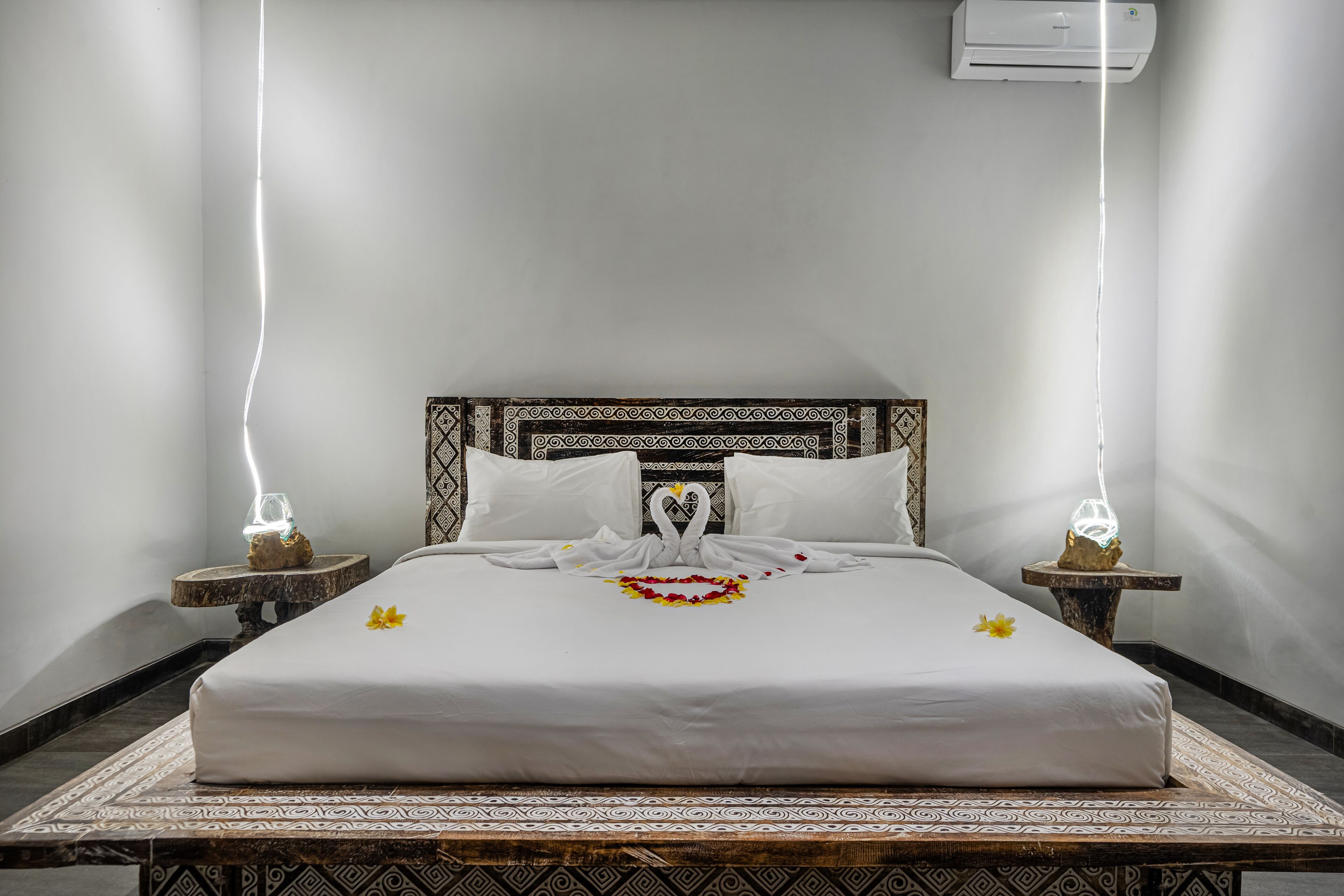 A neatly made bed with a decorative swan design on the pillows, a white bedspread, and a small table with a flower centerpiece.