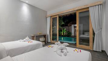 A hotel room with two beds, a small table, and a view of a swimming pool.