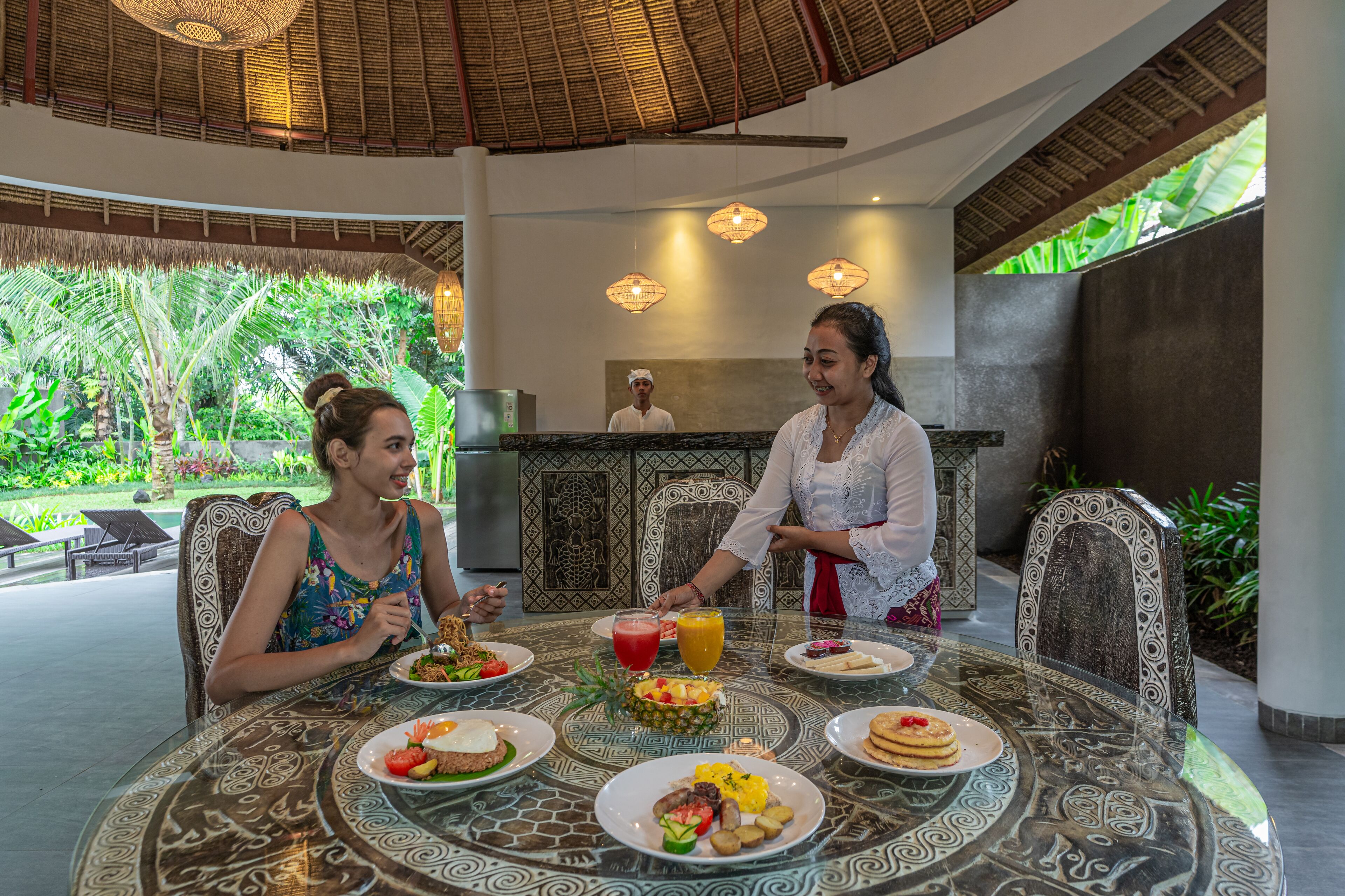 A dining area with a thatched roof, a buffet table with various dishes, and a person serving food.