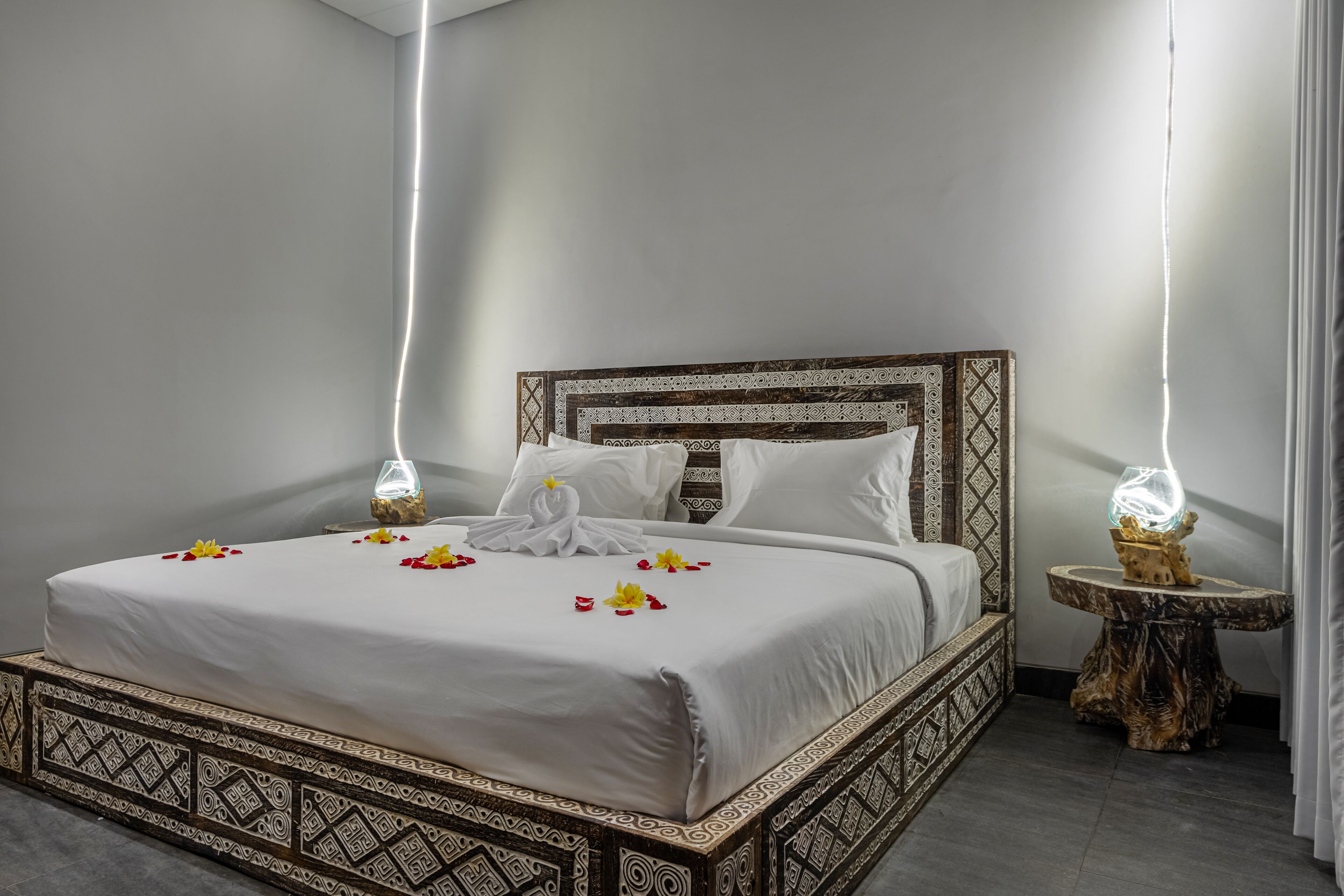 A neatly made bed with a patterned headboard, two bedside tables with decorative lamps, and a simple, clean room design.