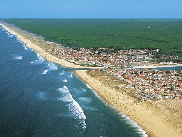 An aerial view of a coastal town with a beach, residential areas, and a large green field.