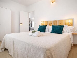 Un lit bien fait, recouvert d’une courtepointe blanche, avec deux coussins turquoise et une petite plante posée sur le lit.