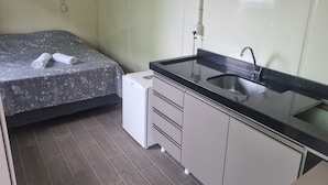 A compact room with a bed, a small refrigerator, and a sink. - Pousada Vila Verde Containers (Barra Velha)