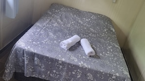 A small, neatly made bed with a floral-patterned bedspread and two rolled towels on it. - Pousada Vila Verde Containers (Barra Velha)