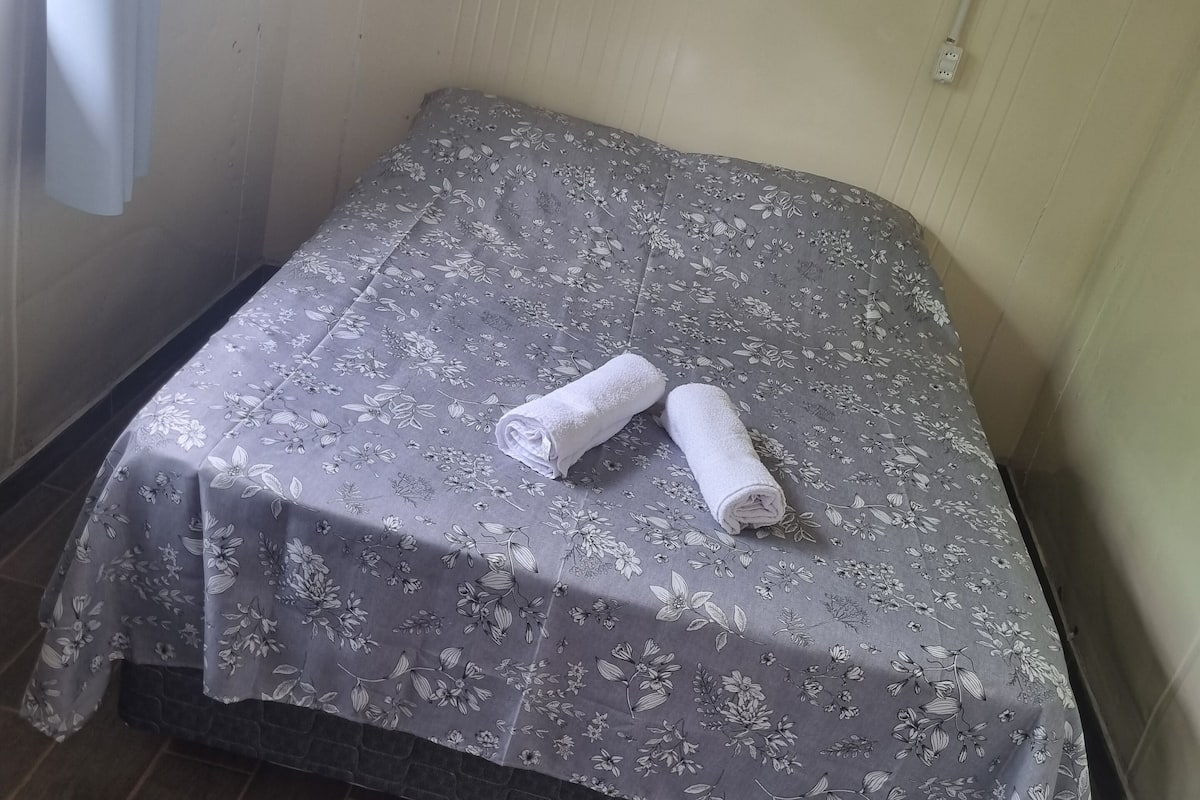 A small, neatly made bed with a floral-patterned bedspread and two rolled towels on it.