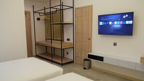 A bedroom with two beds, a TV mounted on the wall, a wardrobe, and a shelf unit.