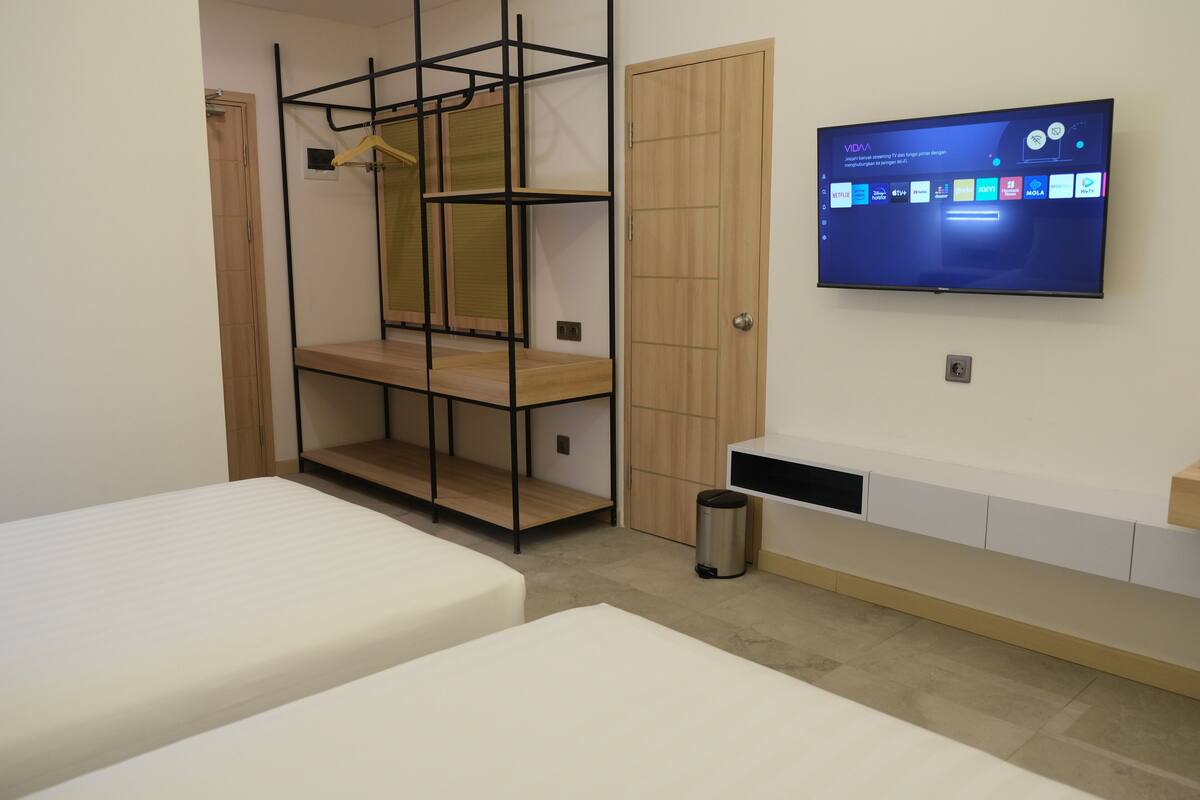 Un dormitorio con dos camas, televisor montado en la pared, armario y estantería.