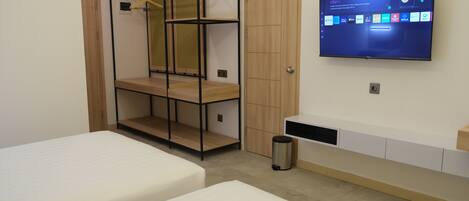 A bedroom with two beds, a TV mounted on the wall, a wardrobe, and a shelf unit.