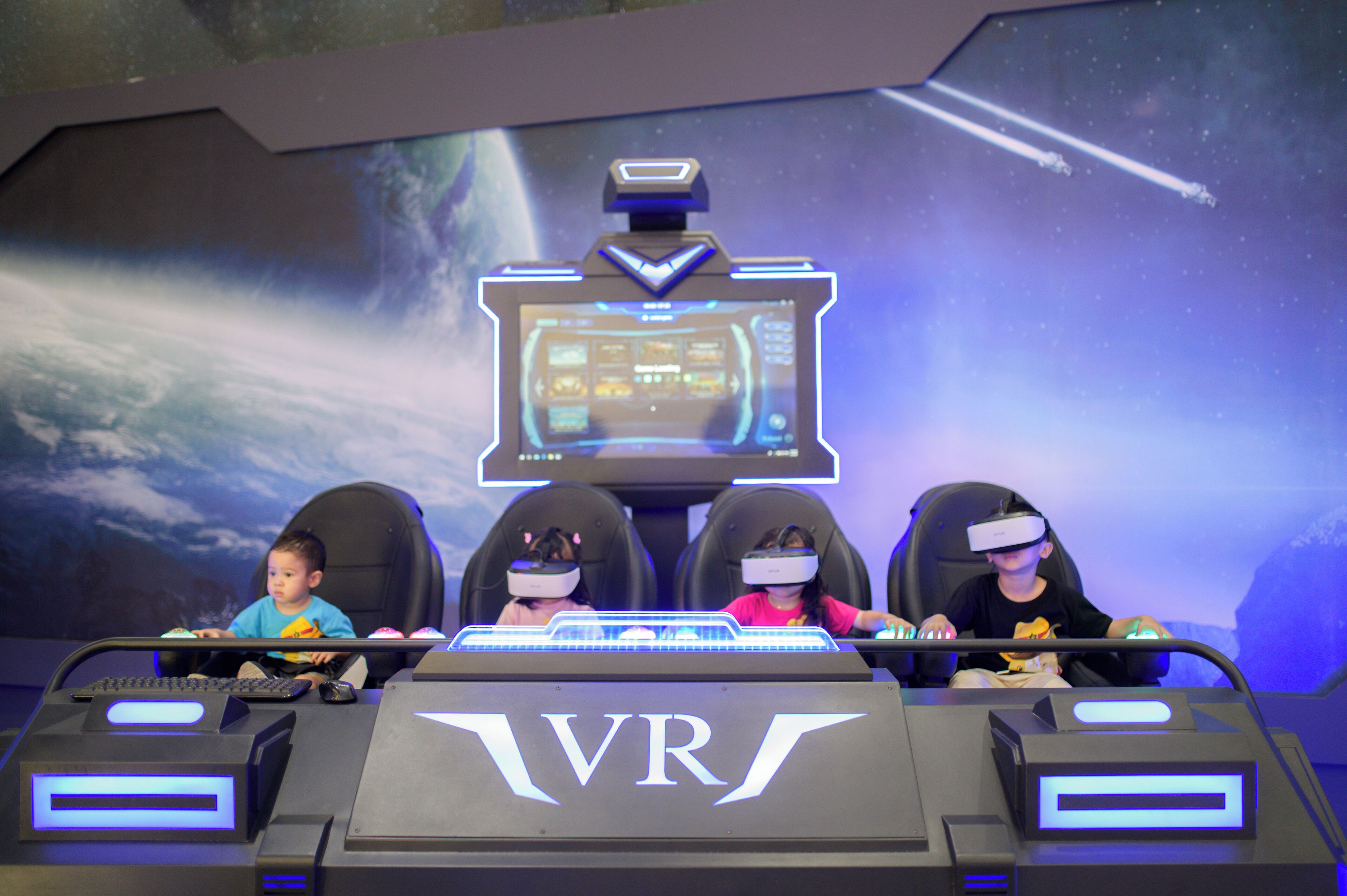 A VR gaming setup with four chairs and a large screen displaying a space-themed game.