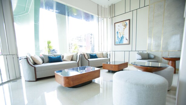 A modern living room with a sofa, ottoman, and coffee table, large windows, and a painting on the wall.