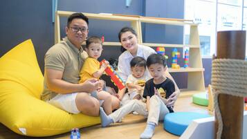 A family sitting on a yellow bean bag in a room with wooden flooring, a bookshelf, and a window.