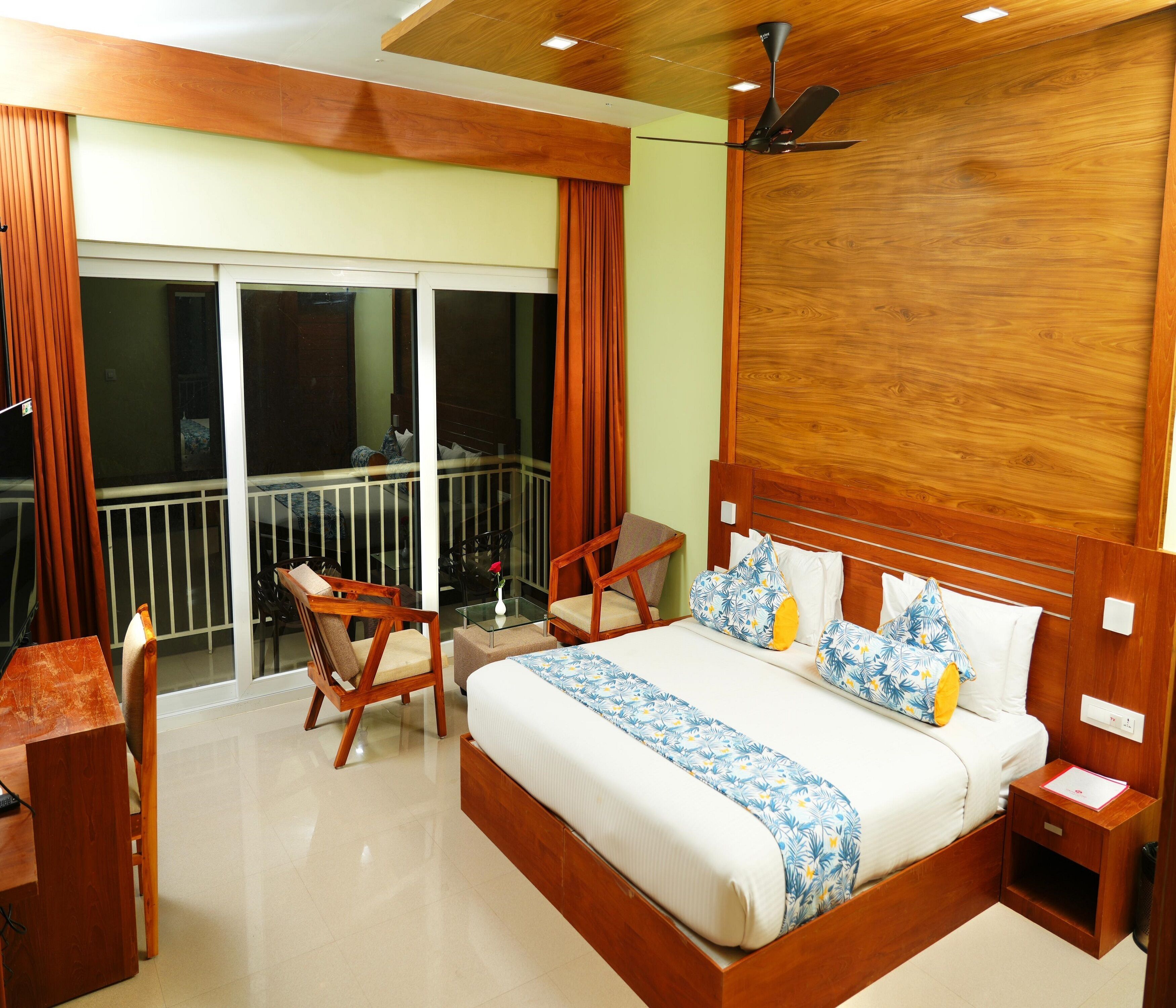 A hotel room with a large bed, wooden headboard, a balcony with a view, a desk, and a chair.