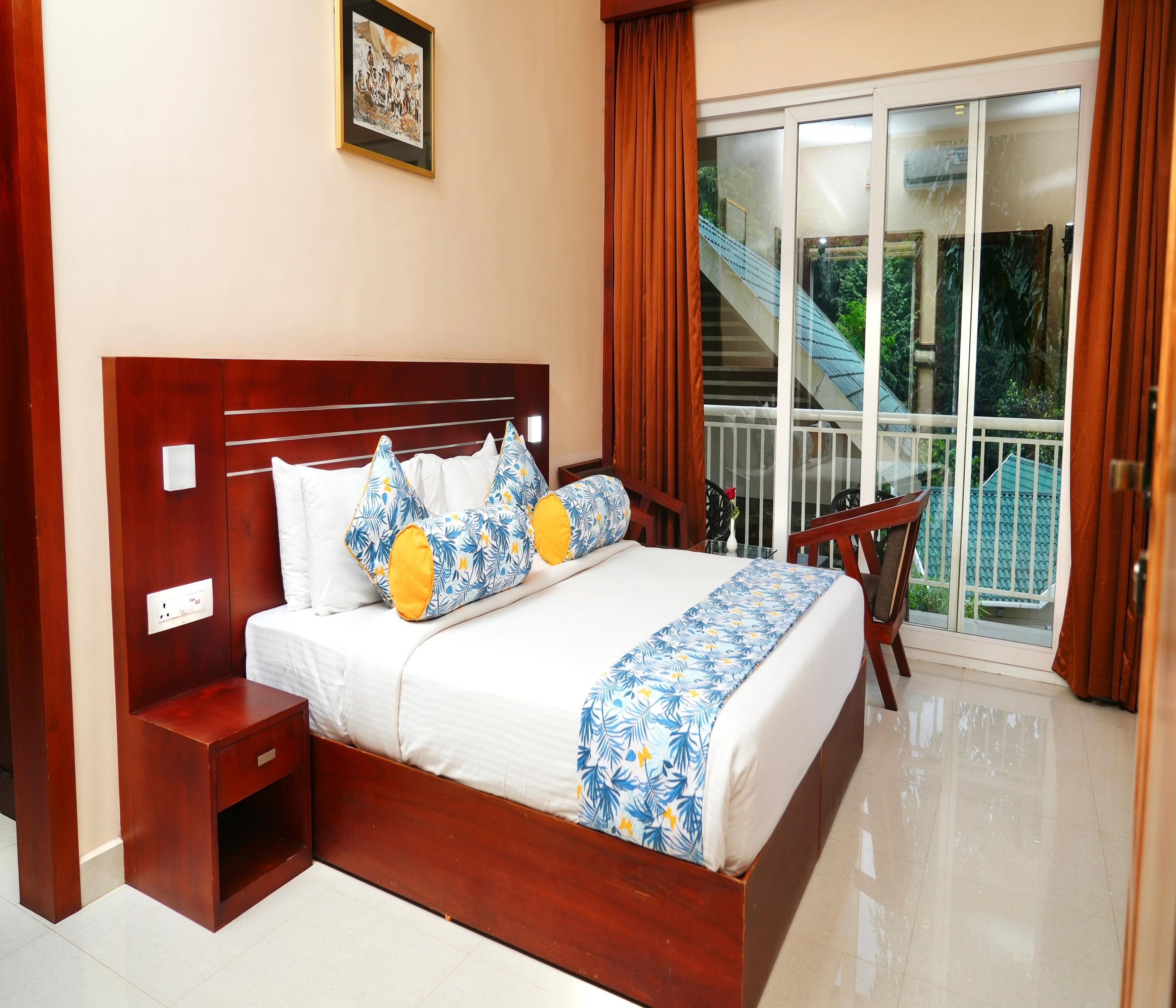 A hotel room with a wooden bed, white bedding, a small bedside table, a chair, and a view of a balcony with a railing.