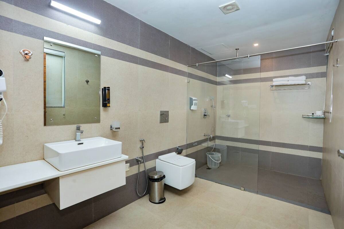 A modern bathroom with a large mirror, a white sink, a glass shower enclosure, and a trash bin.