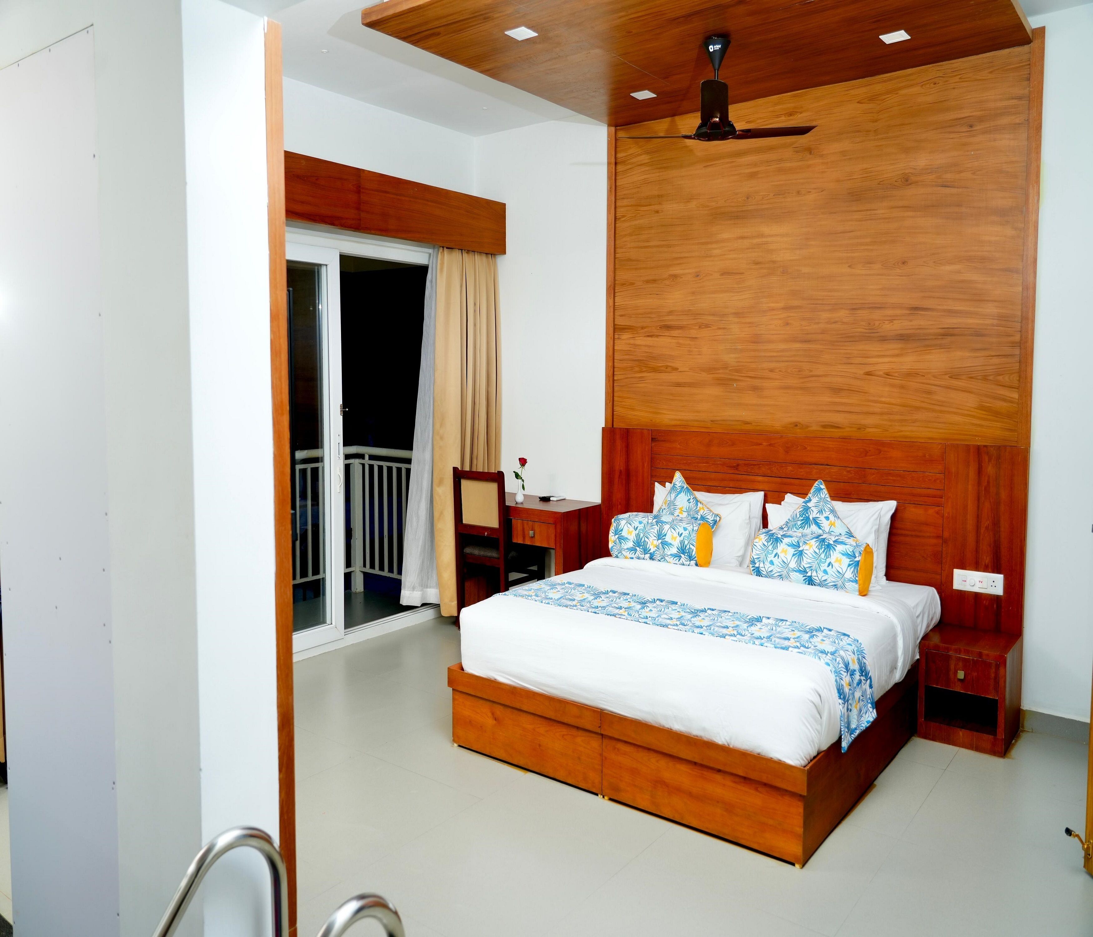 A bedroom with a wooden headboard, a bed with white bedding and blue floral patterns, a nightstand, and a ceiling fan.
