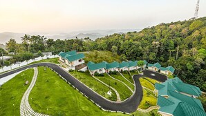 An aerial view of a resort with multiple buildings, a winding road, and lush greenery. - Aveda Munnar Mountains and Mist (Devikolam)